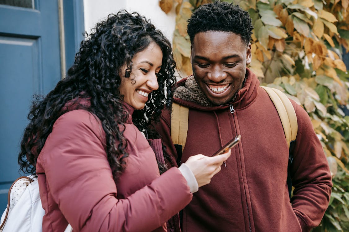 Two people smiling while sharing photos on a smartphone together